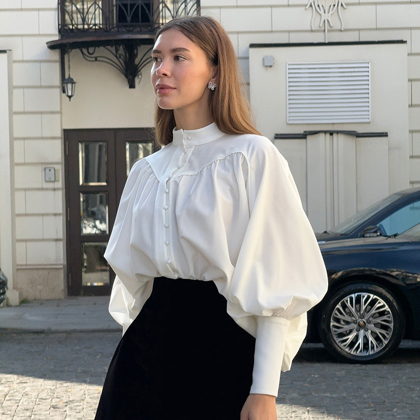 Frau in eleganter weißer Bluse mit Puffärmeln steht vor einem Gebäude. Modetrend, stilvolle Damenmode, zeitlose Eleganz, urbane Kulisse.