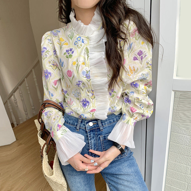 Frau in geblümter Bluse mit Rüschen und blauen Jeans, hält eine Strohtasche. Modetrend, Frühlingsoutfit, feminine Kleidung, Blumenmuster.