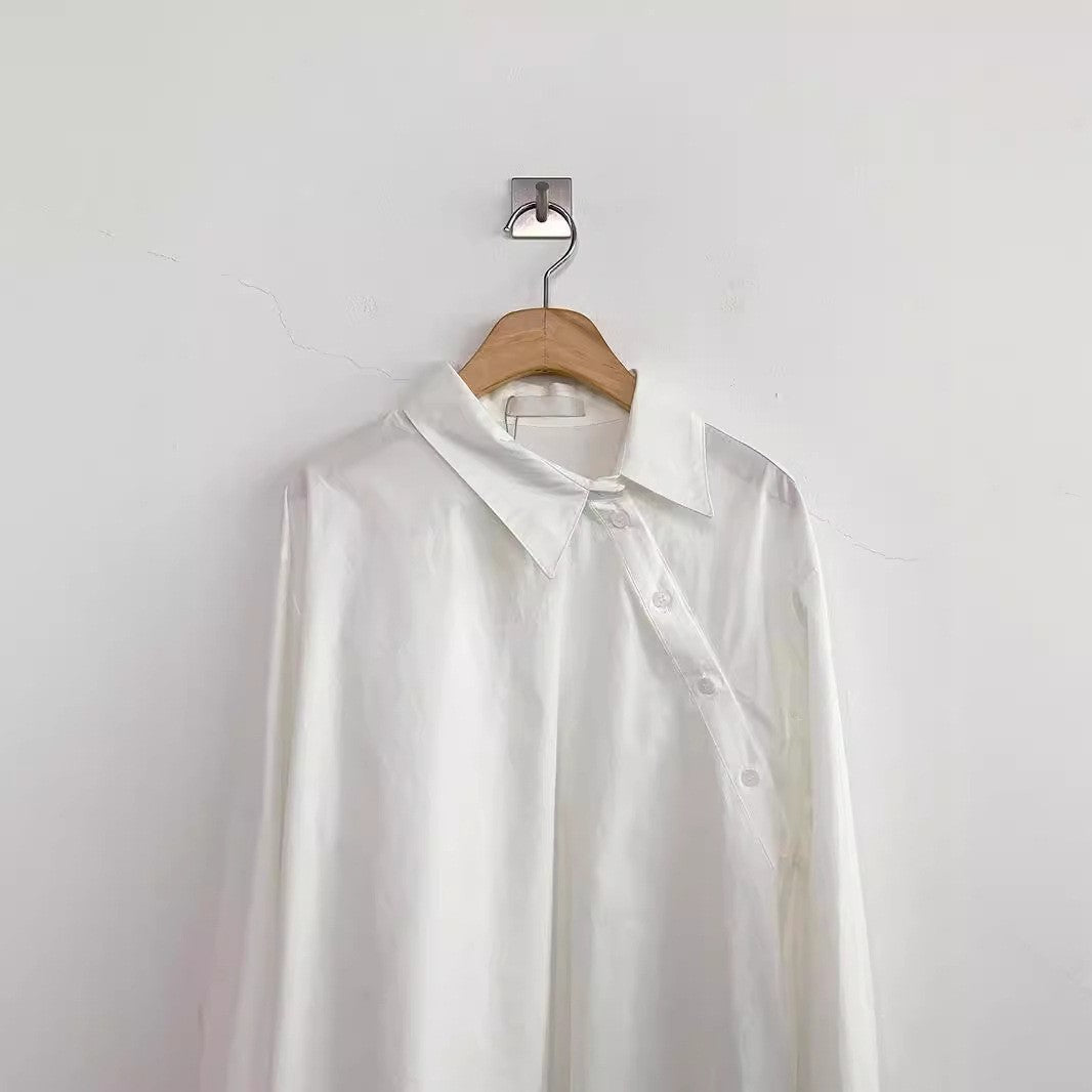 Weiße Bluse aus Seide auf Holzbügel, minimalistisch an weißer Wand aufgehängt. Elegante Damenmode, zeitloses Design, hochwertige Stoffe.