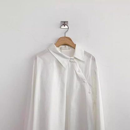 Weiße Bluse aus Seide auf Holzbügel, minimalistisch an weißer Wand aufgehängt. Elegante Damenmode, zeitloses Design, hochwertige Stoffe.