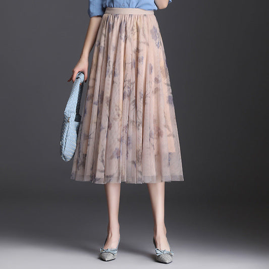 Frau in blauem Hemd und langem, blumigem Tüllrock, hält eine blaue Tasche. Elegante Mode, Damenbekleidung, stilvoller Look.
