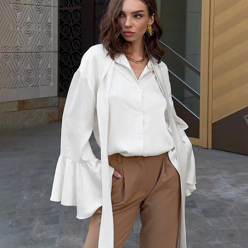 Frau in eleganter weißer Bluse mit Glockenärmeln und brauner Hose, steht vor modernem Gebäude. Modetrend, Damenmode, stilvolle Kleidung.