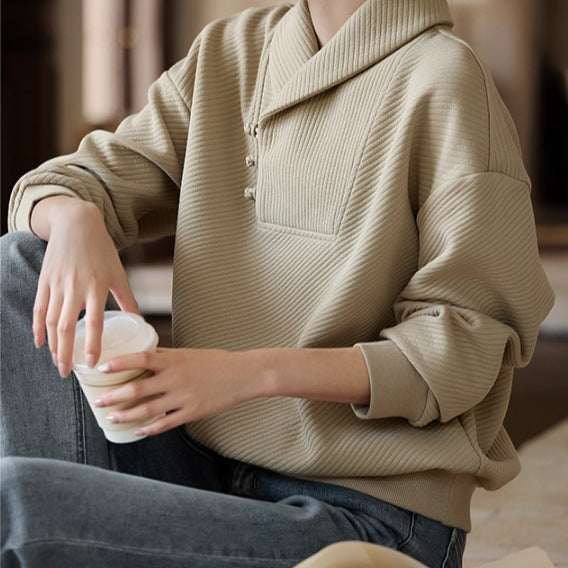 Person in beigem Pullover hält weißen Kaffeebecher, sitzt entspannt auf Sofa. Modetrend, Freizeitkleidung, gemütlicher Look, Innenraum.