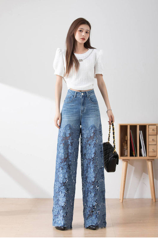 Frau in weißem Oberteil und blauer Spitzen-Jeanshose, steht in modernem Raum. Modetrend, Damenmode, weite Jeans, stilvolle Kleidung.