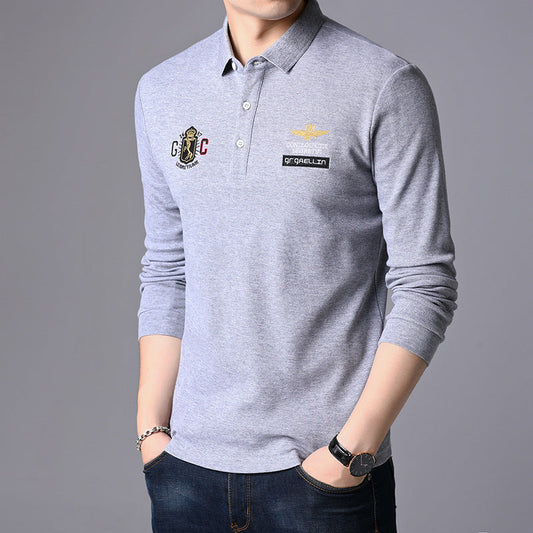Graues Herren-Poloshirt mit langen Ärmeln, besticktem Logo und Emblem, kombiniert mit blauer Jeans. Elegante Freizeitmode für Männer.