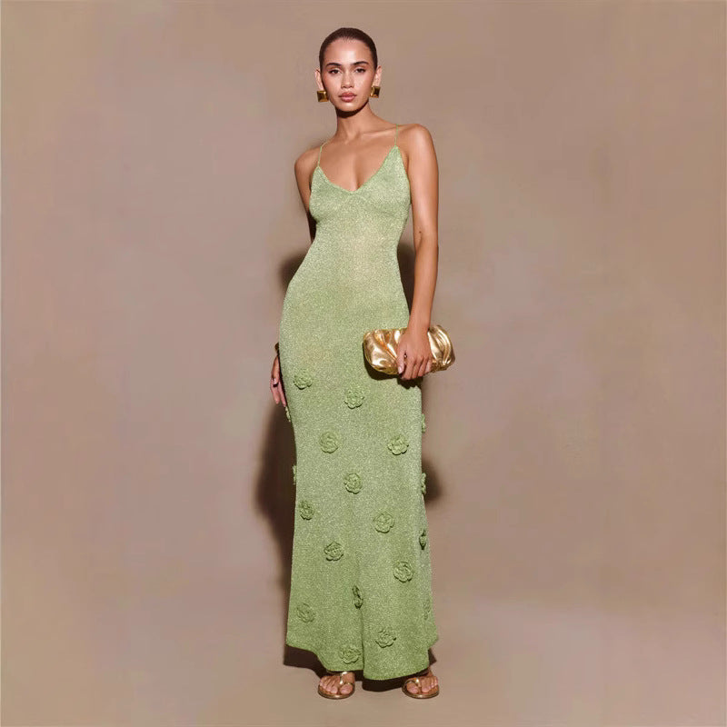 Frau in eleganter, grüner Abendkleid mit Spaghettiträgern und Blumenmuster, hält goldene Clutch, trägt goldene Ohrringe und Sandalen.