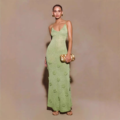 Frau in eleganter, grüner Abendkleid mit Spaghettiträgern und Blumenmuster, hält goldene Clutch, trägt goldene Ohrringe und Sandalen.