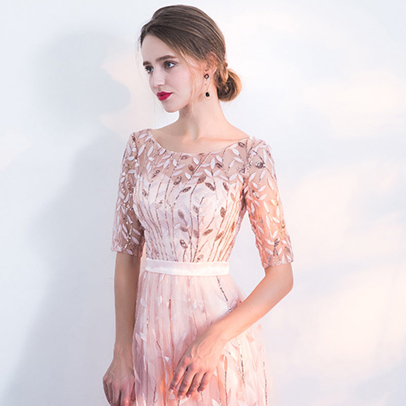 Frau in elegantem, rosa Abendkleid mit floralen Stickereien, schulterfreiem Design und halblangen Ärmeln. Perfekt für formelle Anlässe und Hochzeiten.