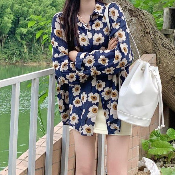 Frau in geblümter Bluse und gelbem Rock steht am Seeufer, trägt weiße Tasche. Sommermode, Freizeitkleidung, Naturhintergrund.