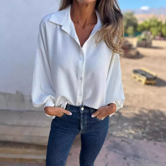 Frau in weißer Bluse und blauer Jeans, lässig stehend mit Händen in den Taschen, draußen bei sonnigem Wetter. Mode, Freizeitkleidung, Damenoutfit.