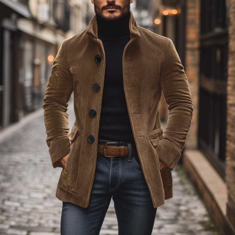 Mann in braunem Cordmantel und schwarzem Rollkragenpullover auf Kopfsteinpflasterstraße. Modischer Herbstlook, stilvolle Herrenmode, urbane Kulisse.