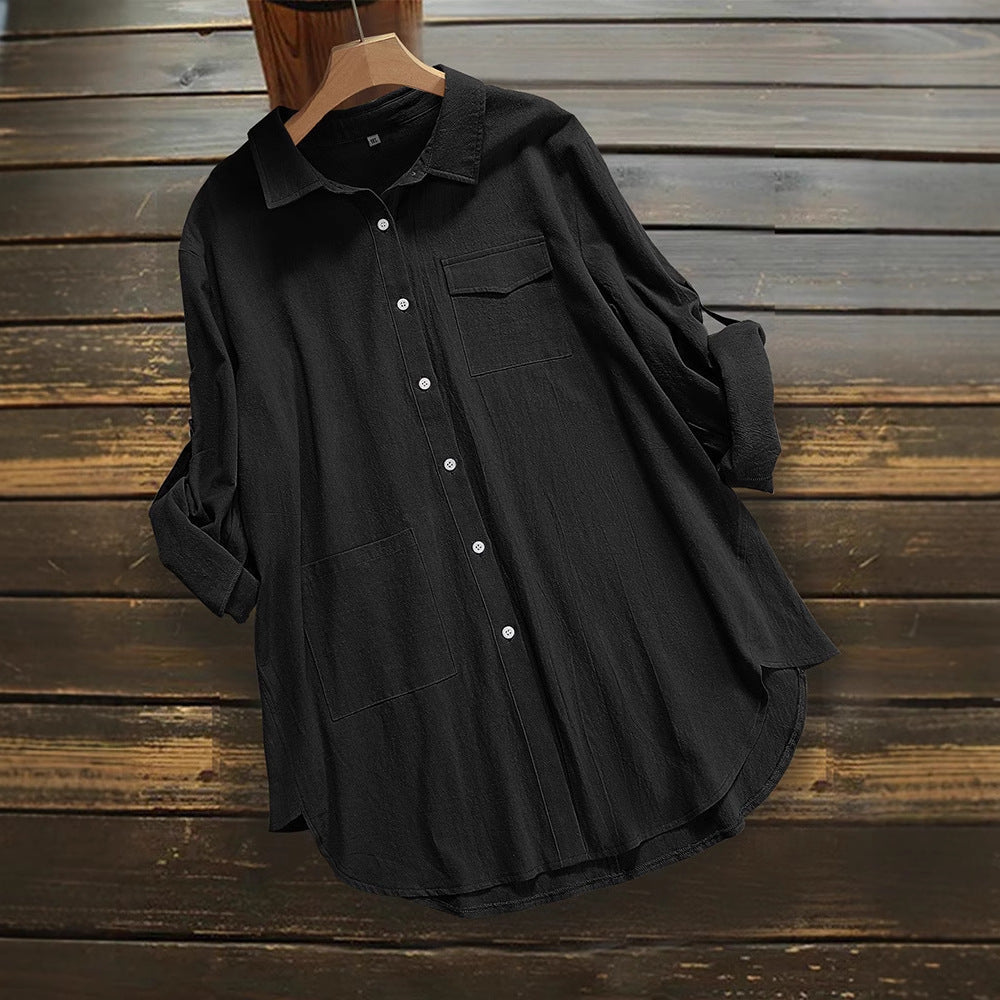 Schwarze Damenbluse aus Baumwolle mit Knopfleiste und Brusttasche, lässiger Stil, hängend auf Holzkleiderbügel vor rustikalem Holzhintergrund.