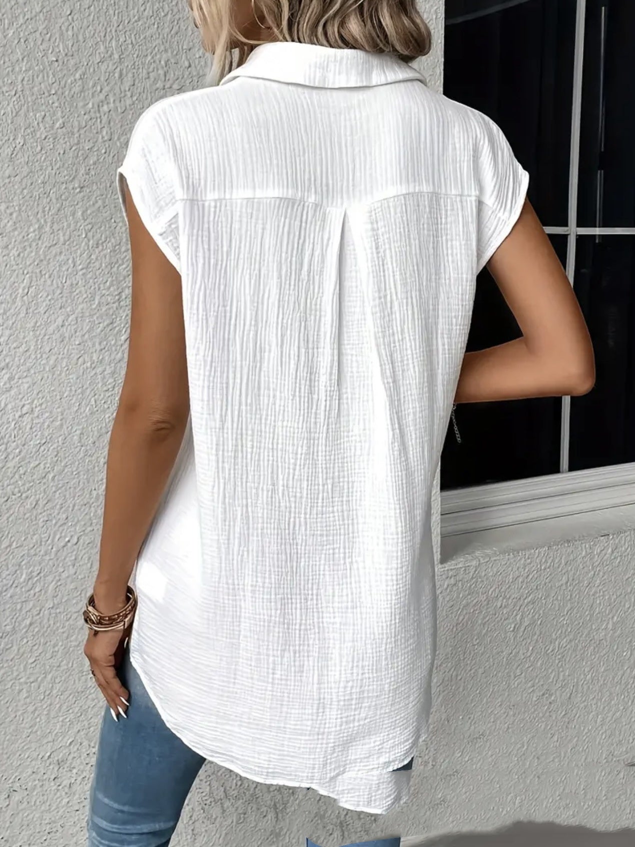 Frau in weißer, ärmelloser Bluse aus Baumwolle, Rückansicht, vor grauer Wand. Modetrend, Sommeroutfit, lässiger Stil.
