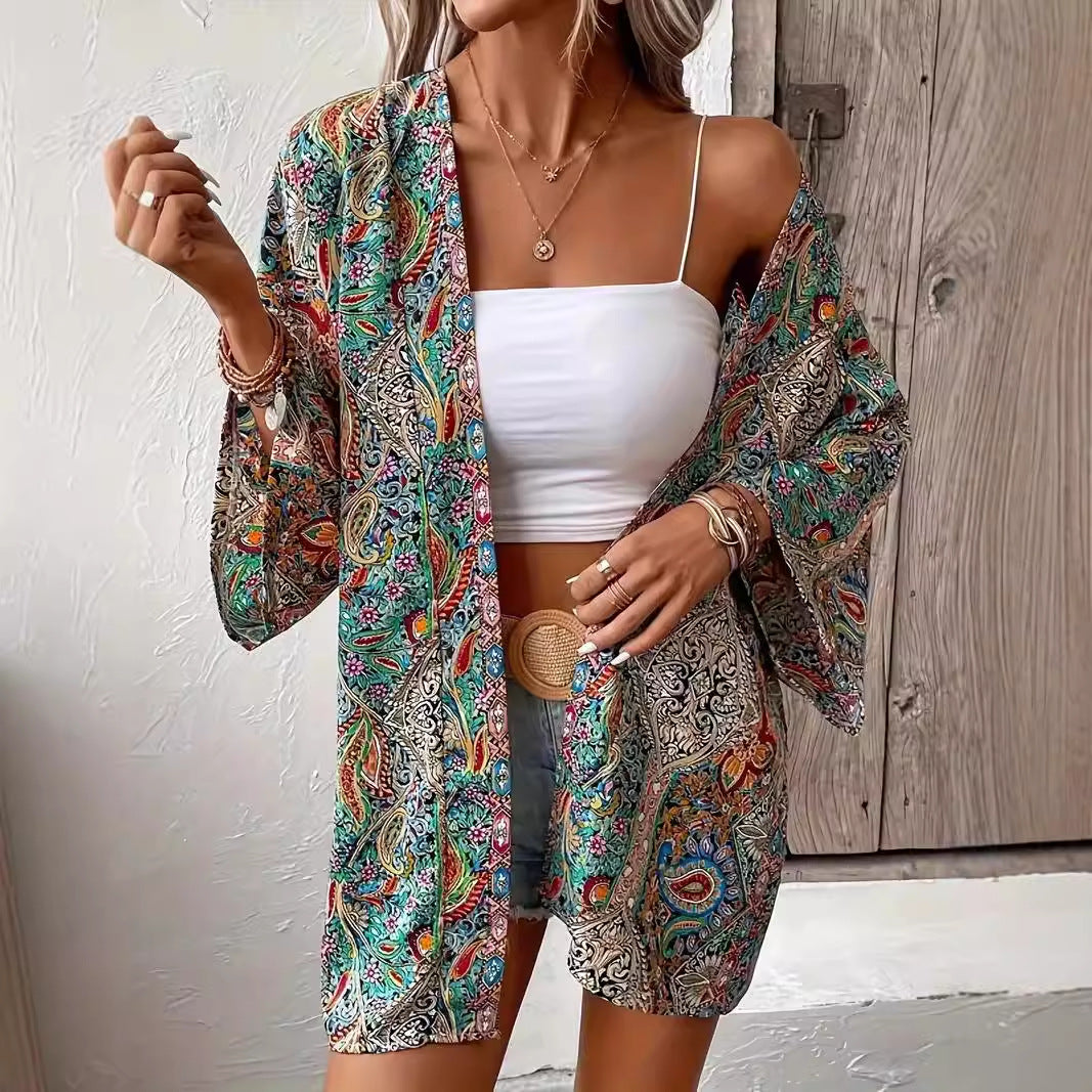 Frau in buntem Kimono, weißem Crop-Top und Jeansshorts vor Holztür. Sommermode, Boho-Stil, lässiges Outfit, modische Accessoires.