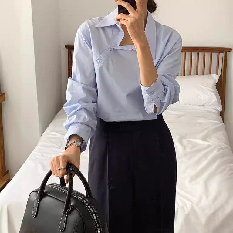 Frau in hellblauer Bluse und schwarzem Rock steht in Schlafzimmer, hält schwarze Ledertasche und Smartphone. Elegante Businessmode, minimalistisch.