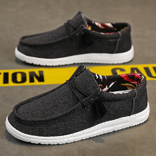 Dunkelgraue Freizeitschuhe mit weißer Sohle, floralem Innenfutter, auf Betonboden vor gelbem "Caution"-Band. Ideal für Herrenmode und Streetwear.
