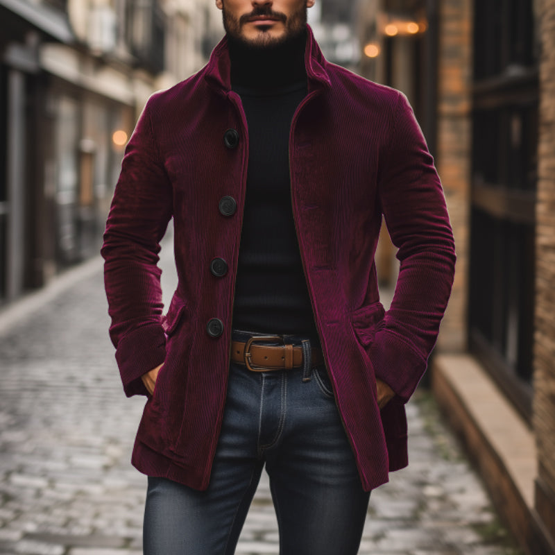Mann in bordeauxrotem Cordmantel, schwarzem Rollkragenpullover und Jeans auf gepflasterter Straße. Modischer Herbstlook, urbane Herrenmode.