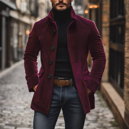 Mann in bordeauxrotem Cordmantel, schwarzem Rollkragenpullover und Jeans auf gepflasterter Straße. Modischer Herbstlook, urbane Herrenmode.