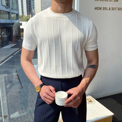 Mann in weißem, geripptem T-Shirt hält Tasse, trägt schwarze Hose und goldene Uhr. Moderne, minimalistische Umgebung. Mode, Herrenbekleidung.