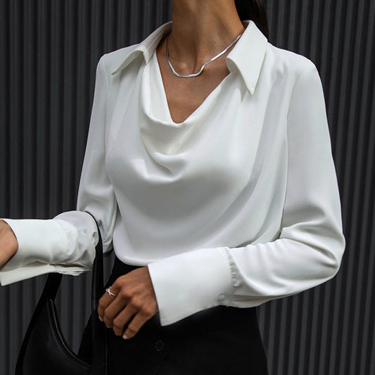 Elegante Frau in weißer Bluse mit Wasserfallausschnitt, trägt silberne Halskette und schwarze Tasche. Businessmode, stilvoll, modern.