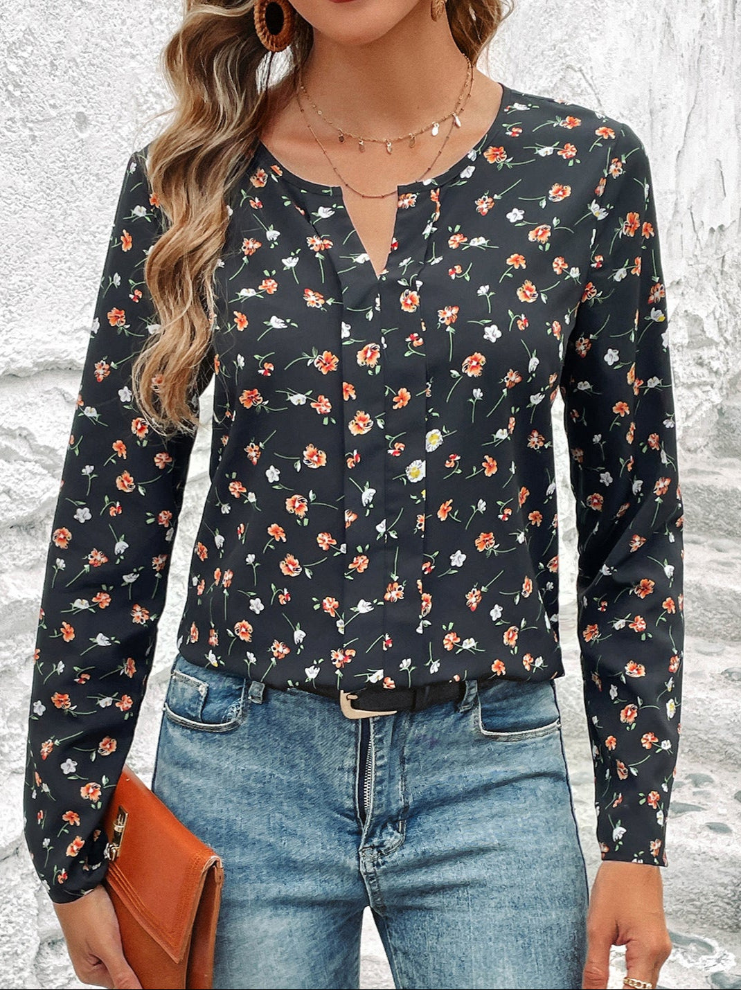 Frau in geblümter Bluse und Jeans, hält braune Clutch. Modetrend, Damenmode, lässiger Look, florales Muster, Streetstyle.