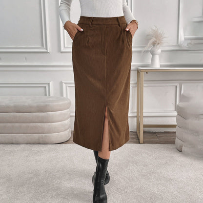 Frau in braunem Cordrock mit Schlitz, weißem Pullover und schwarzen Stiefeln in elegantem Wohnzimmer. Modetrend, Herbstmode, Damenbekleidung.