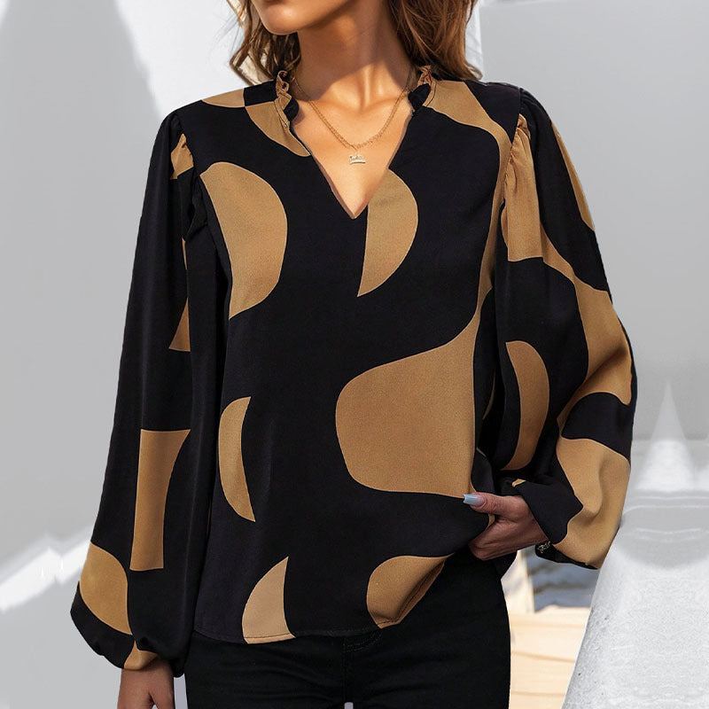 Frau trägt stilvolle schwarze Bluse mit goldenen abstrakten Mustern, V-Ausschnitt und langen Ärmeln. Elegante Mode, trendiges Design.
