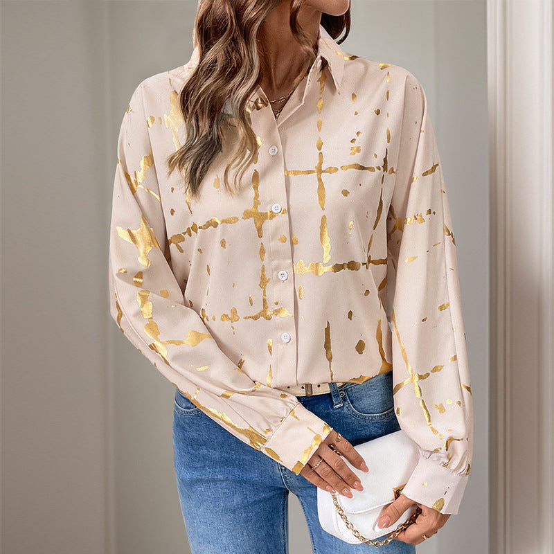 Frau in eleganter, beige-goldener Bluse mit abstraktem Muster, kombiniert mit blauen Jeans und weißer Clutch. Modetrend, Damenmode, stilvoll.