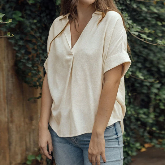 Frau in beiger Bluse und blauer Jeans vor grünem Hintergrund. Modetrend, lässiger Stil, Damenbekleidung, Outdoor-Fotografie.