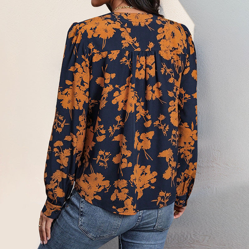 Damenbluse mit orangefarbenem Blumenmuster auf dunkelblauem Hintergrund, langärmlig, kombiniert mit blauen Jeans. Modetrend Herbst 2023.