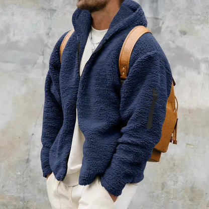 Mann in blauer Fleecejacke mit Kapuze und braunem Rucksack vor grauem Hintergrund. Wintermode, Herrenbekleidung, Outdoor-Look.