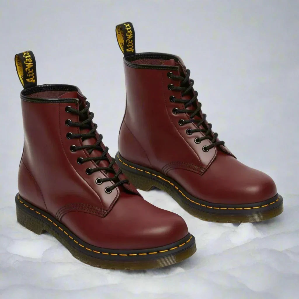 Bordeauxrote Lederstiefel mit gelber Naht und schwarzer Schnürung auf weißem Hintergrund. Robuste, modische Boots für Damen und Herren.