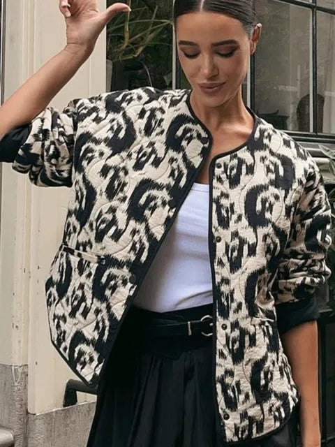 Frau trägt modische Jacke mit schwarz-weißem Leopardenmuster, kombiniert mit weißem Top und schwarzer Hose. Trendige Herbstmode, urbaner Stil.