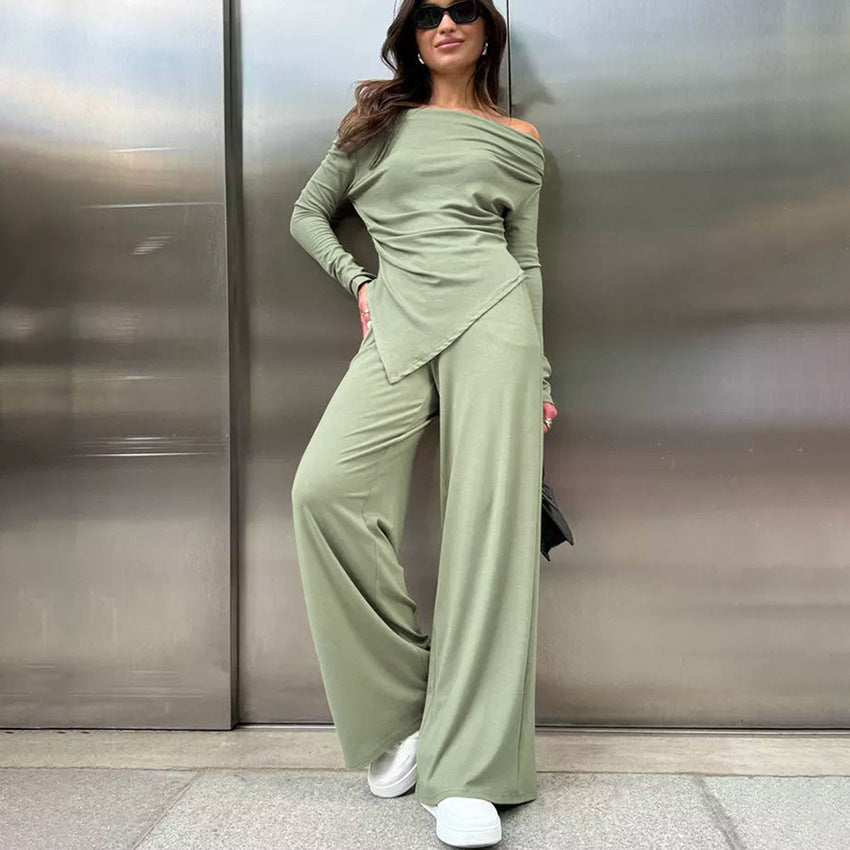 Frau in grünem Off-Shoulder-Jumpsuit und weißen Sneakers vor metallischer Wand. Modetrend, lässiger Stil, Streetwear, Damenmode.