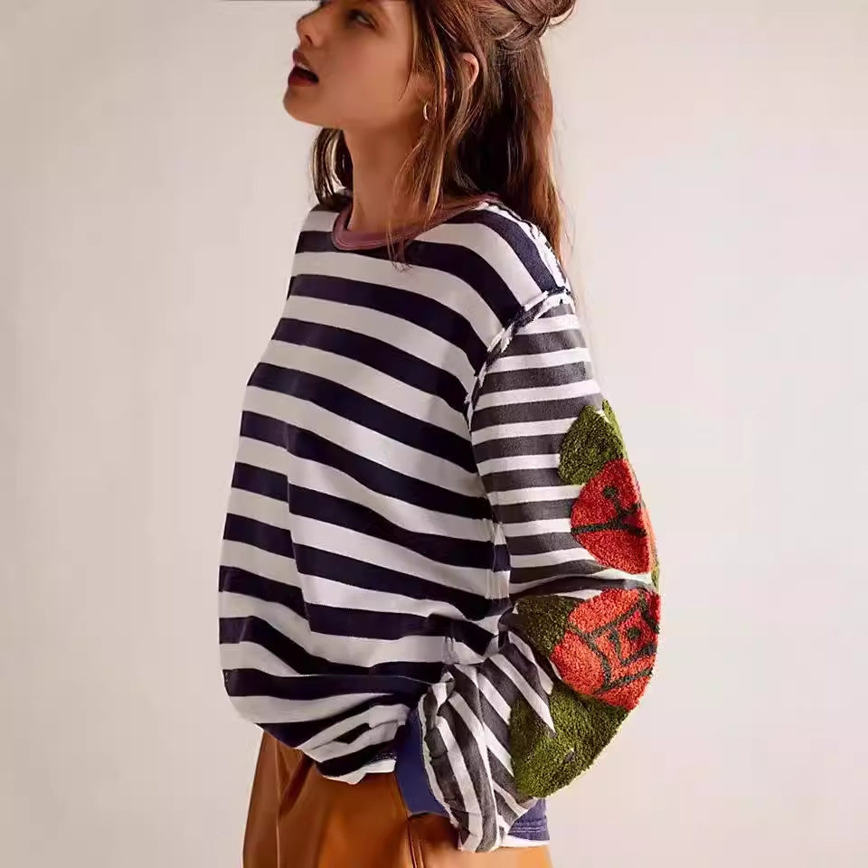 Frau in gestreiftem Pullover mit Blumenmuster auf den Ärmeln, seitlich stehend, lässiger Look, modische Damenbekleidung, trendiger Stil.