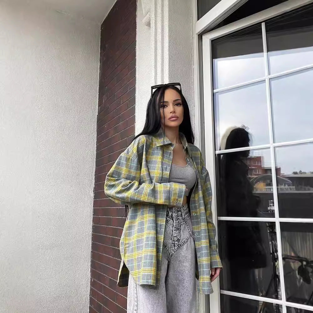 Frau in kariertem Hemd und grauem Top steht auf Balkon vor Glastür. Modetrend, lässiger Look, urbane Kleidung, stilvolle Frau.