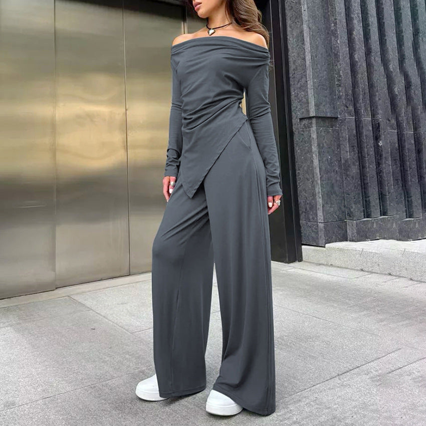 Frau in grauem, schulterfreiem Jumpsuit mit weitem Bein und weißen Sneakers vor moderner Architektur. Elegante Damenmode, Streetstyle.