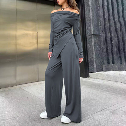 Frau in grauem, schulterfreiem Jumpsuit mit weitem Bein und weißen Sneakers vor moderner Architektur. Elegante Damenmode, Streetstyle.
