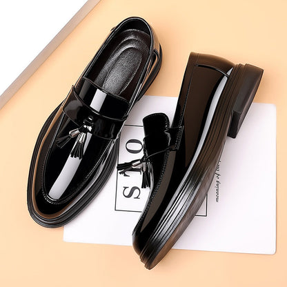 Schwarze Lackleder-Loafer mit Quasten auf beigem Hintergrund, elegante Herrenschuhe, modisches Design, hochwertige Materialien.