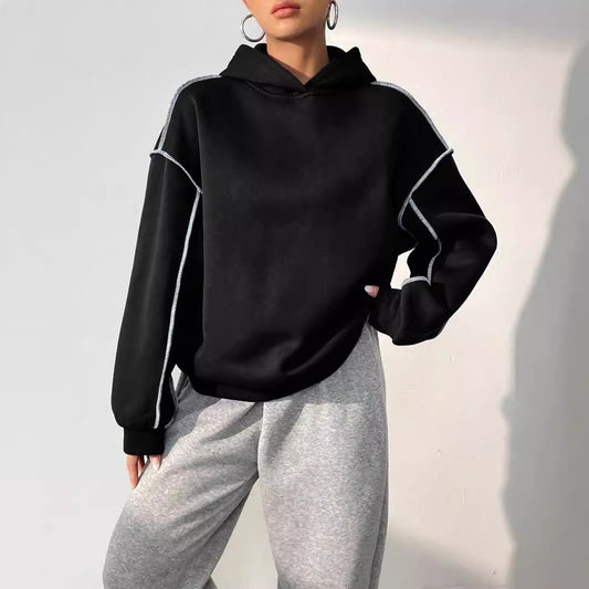 Frau in schwarzem Hoodie mit weißen Streifen und grauer Jogginghose. Modetrend, lässiger Stil, bequeme Freizeitkleidung.