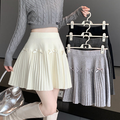 Frau in grauem Strickpullover hält drei Faltenröcke in Weiß, Grau und Schwarz. Modetrend, Damenmode, Herbstkollektion, stilvolle Outfits.