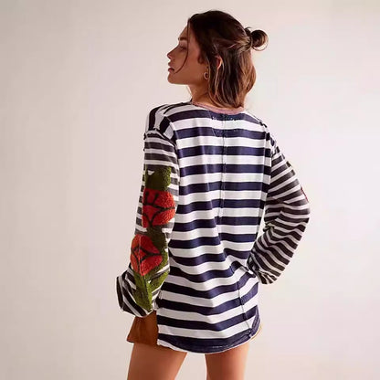 Frau in gestreiftem Pullover mit Blumenmuster auf den Ärmeln, seitlich stehend. Modetrend, Damenmode, lässiger Stil, Herbstmode.