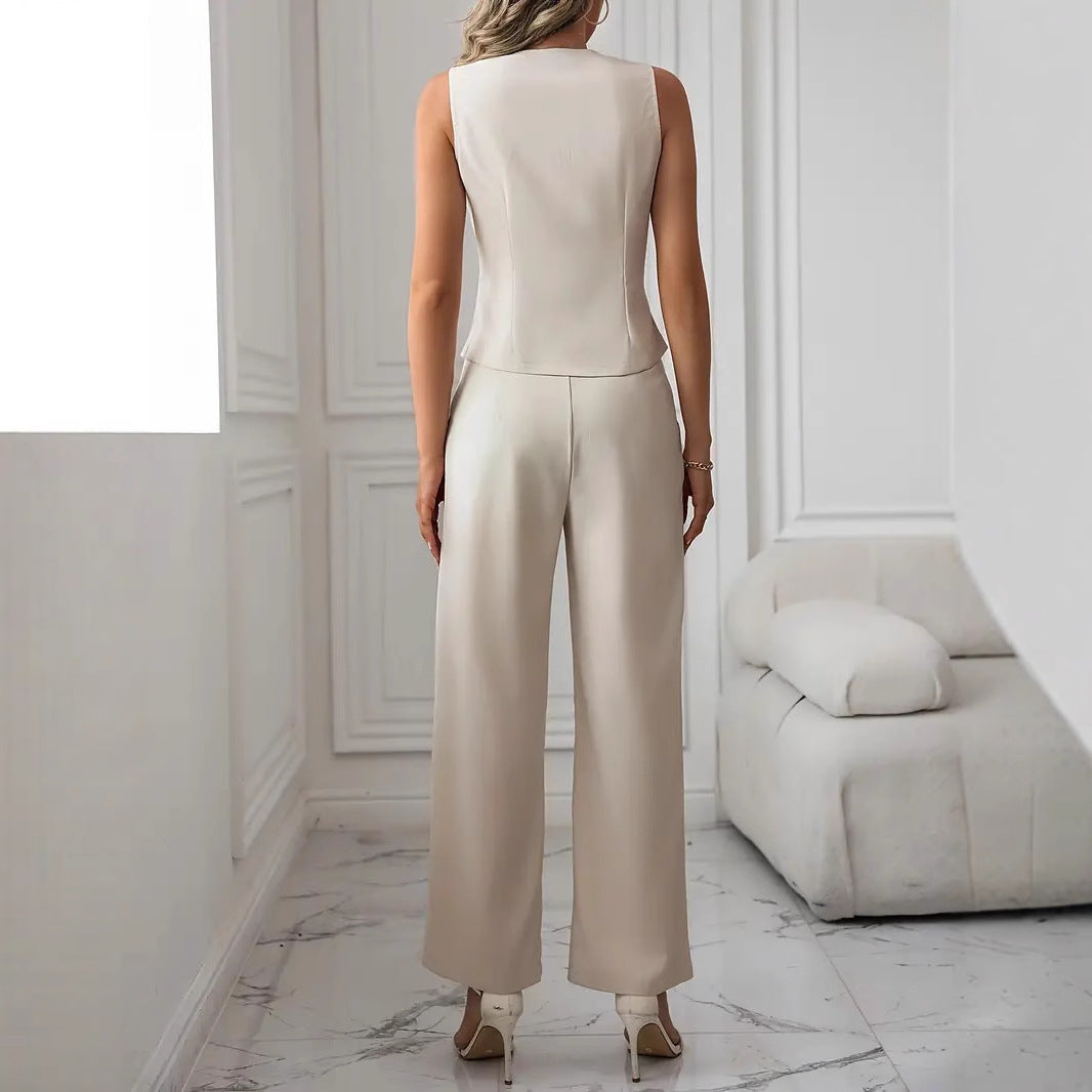 Elegante Frau in cremefarbenem Hosenanzug, steht in modernem, minimalistischem Raum mit weißem Sofa und Marmorboden, stilvolle Mode.
