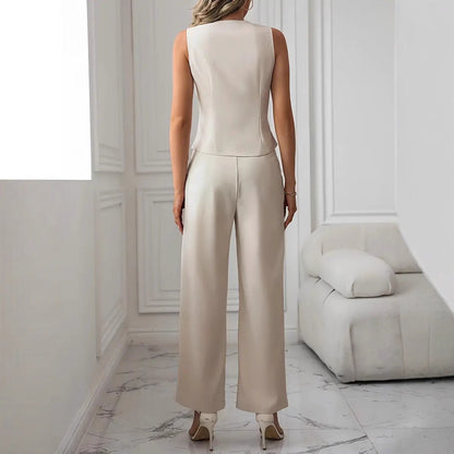 Elegante Frau in cremefarbenem Hosenanzug, steht in modernem, minimalistischem Raum mit weißem Sofa und Marmorboden, stilvolle Mode.