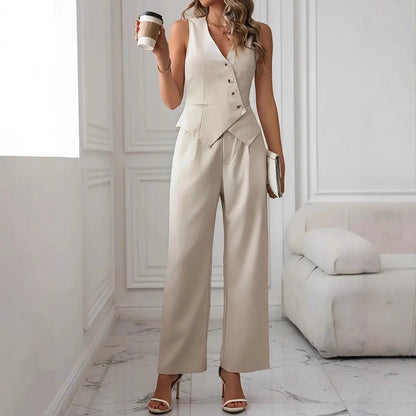 Frau in eleganter, cremefarbener Weste und Hose, hält Kaffeebecher, steht in modernem, minimalistischem Wohnzimmer mit weißem Sofa.