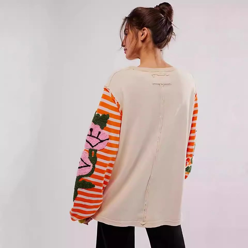 Frau in modischem Pullover mit gestreiften Ärmeln und Blumenmuster, Rückansicht. Trendige Damenmode, lässiger Stil, Herbstkollektion.