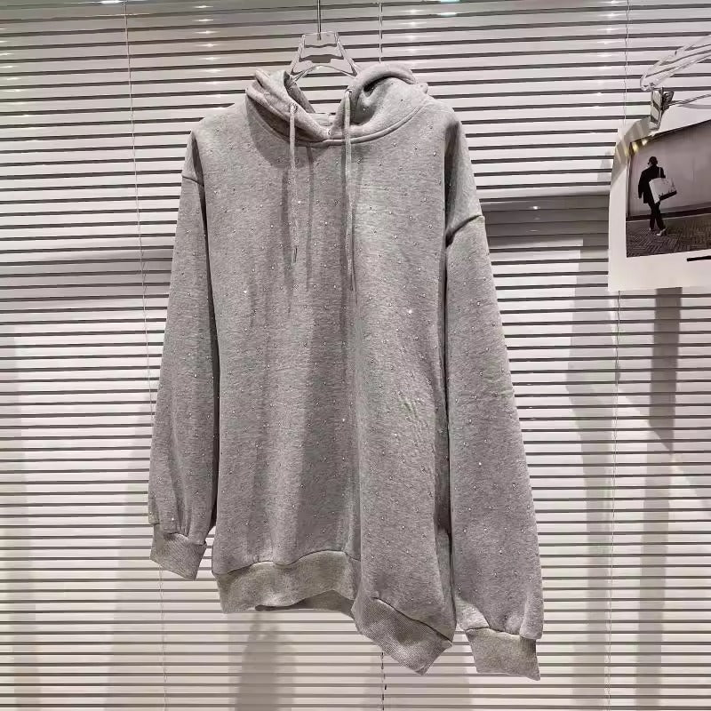 Grauer Kapuzenpullover aus Baumwolle, hängend vor weißen Jalousien. Bequeme Freizeitmode, ideal für Herbst und Winter. Minimalistisches Design.