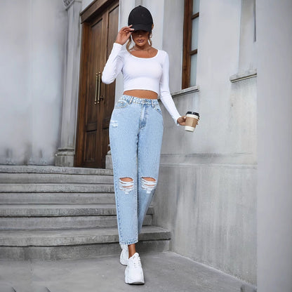 Frau in zerrissenen Jeans und weißem Crop-Top, trägt schwarze Kappe und weiße Sneaker, hält Kaffeebecher, geht Treppe hinunter vor grauem Gebäude.