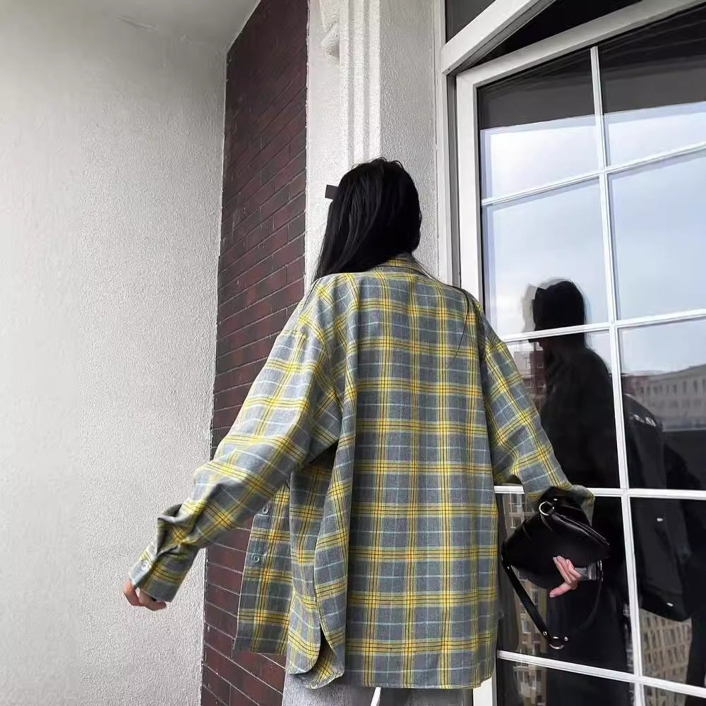 Frau mit kariertem Hemd auf Balkon, hält schwarze Tasche. Mode, Streetstyle, lässiger Look, urbane Kulisse, Fensterreflexion.