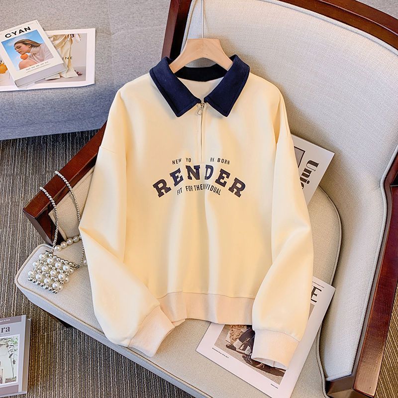 Beige Sweatshirt mit schwarzem Kragen und "Render"-Aufdruck auf einem Sessel, daneben eine Perlenhandtasche und Modezeitschriften.